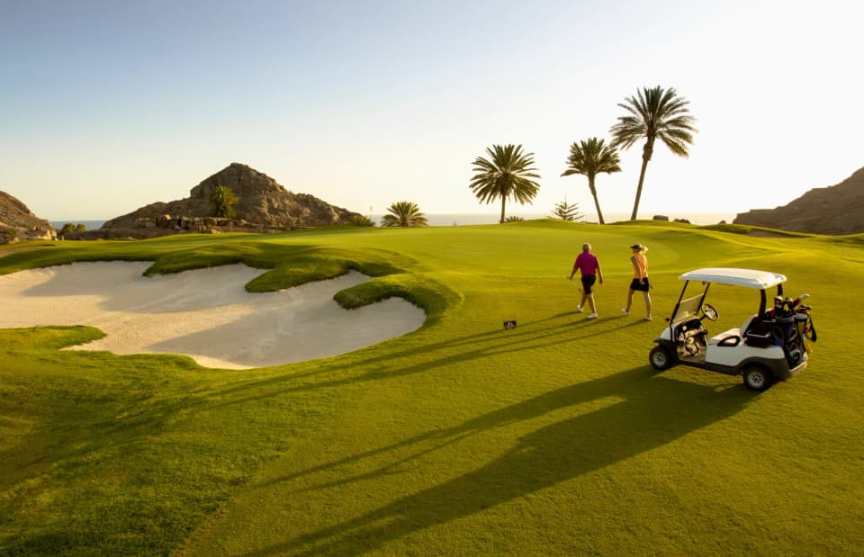 Golfers beside a bunker at Anfi Tauro, with palms and the sea beyond