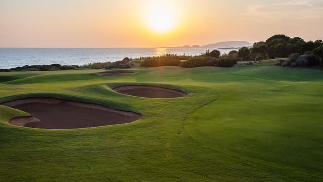 Pot bunkers and a green on the Dunes Course at sunset, with the sea behind