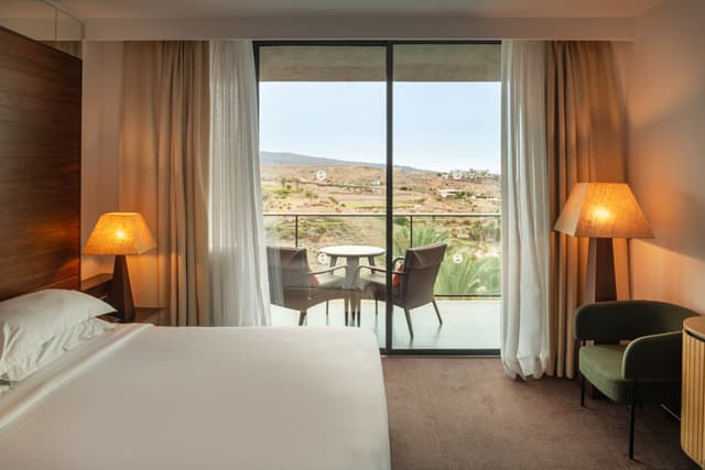 A bright room at Salobre Hotel with a glass wall onto the terrace and hills