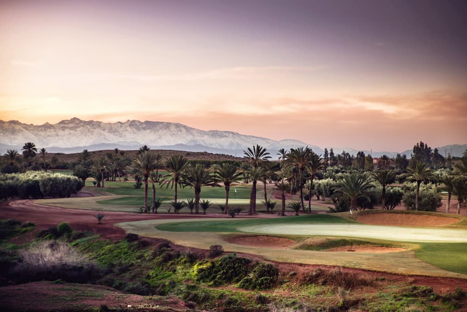 A green at Assoufid beside a desert canyon, with the snowy Atlas behind