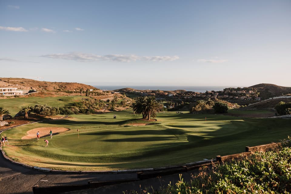 Golfers on a green at Salobre Golf, with palms and the Atlantic beyond